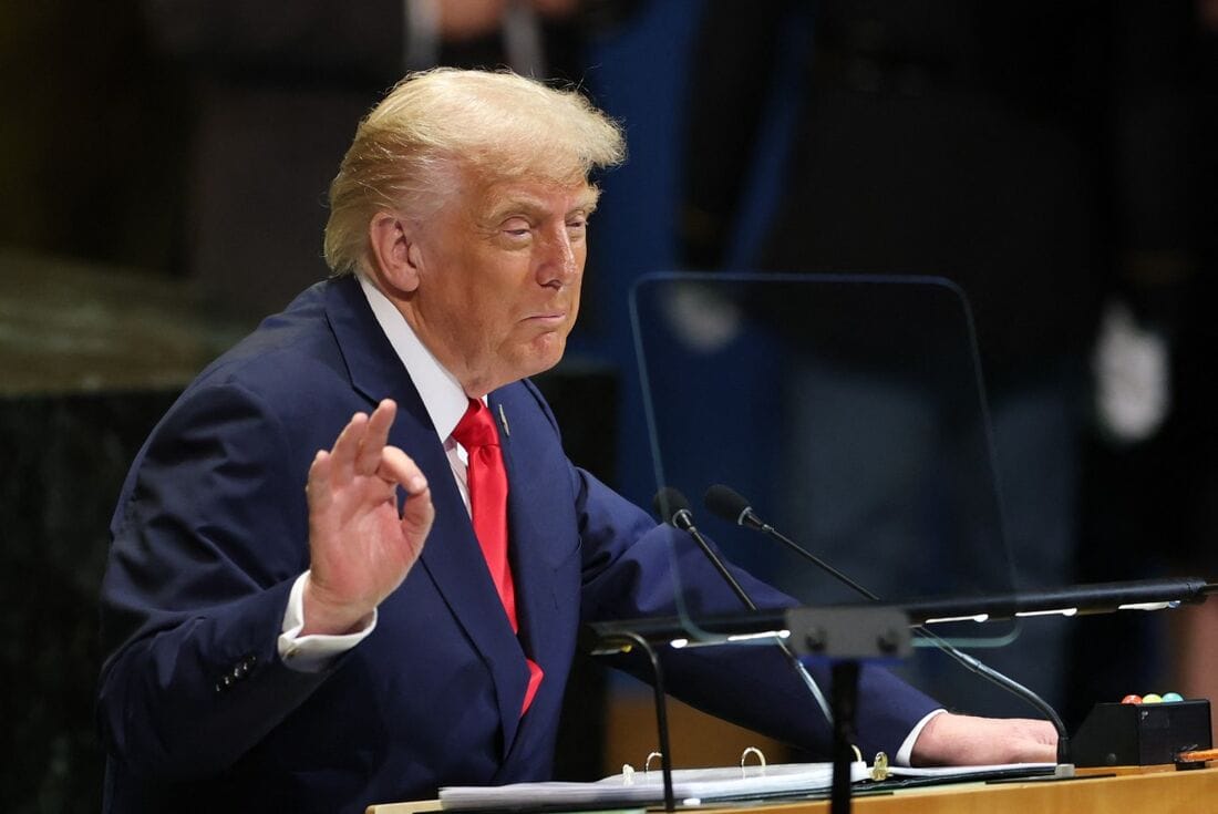Donald Trump em pé atrás de um púlpito com microfones, gesticulando durante um discurso
