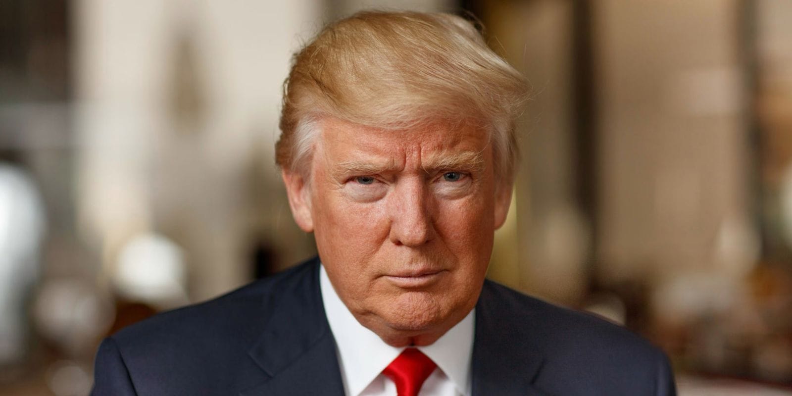 O presidente Donald Trump, de terno escuro e gravata vermelha, em retrato aproximado, com o fundo desfocado