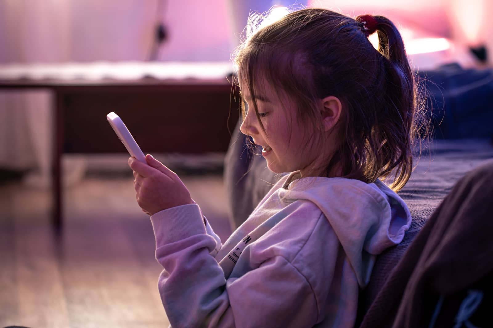 Criança sorrindo enquanto mexe no celular, sentada em um sofá