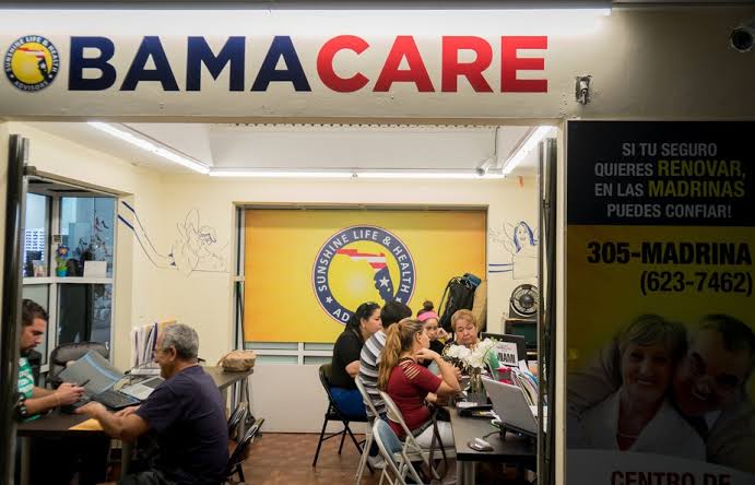 Pessoas usam notebooks em um posto de atendimento com o letreiro Obamacare e um cartaz em espanhol