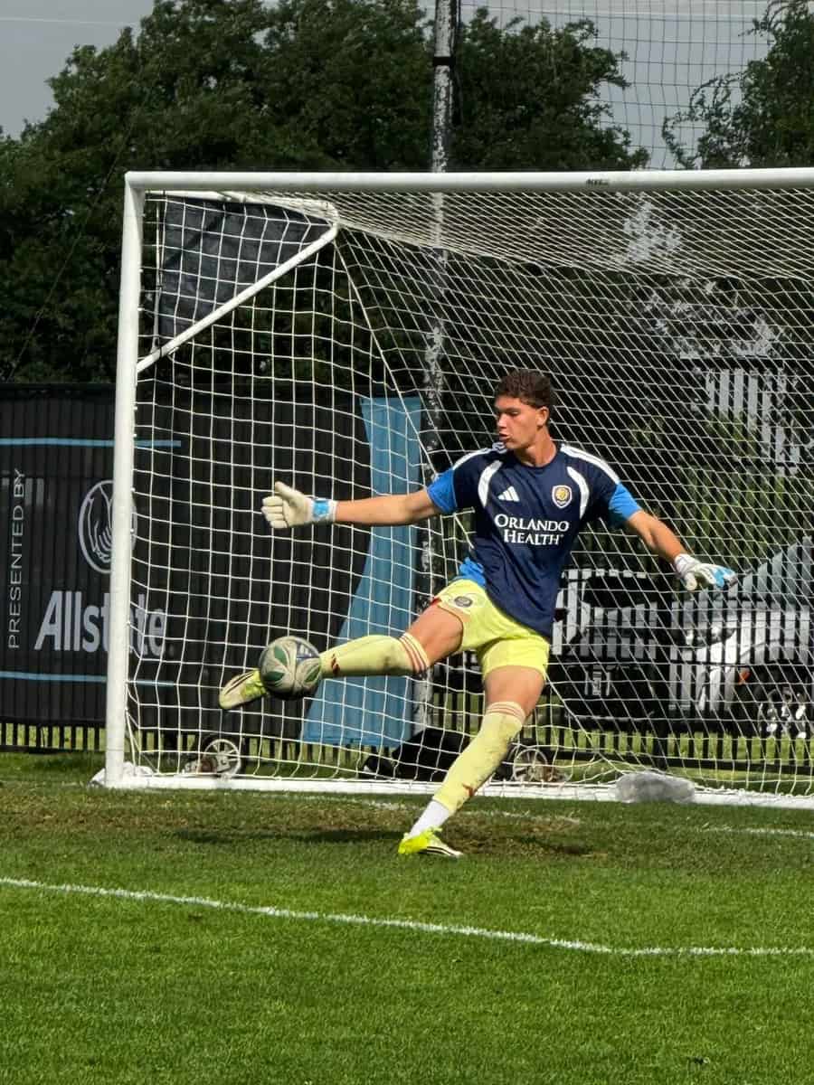 Goleiro de camisa azul-marinho do Orlando City e calção amarelo bate na bola dentro da pequena área, diante do gol com a rede branca