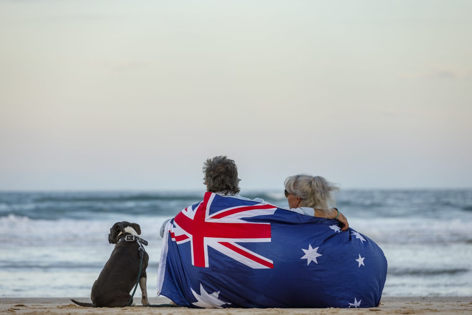 Casal com bandeira da Austrália e cachorro sentados numa praia