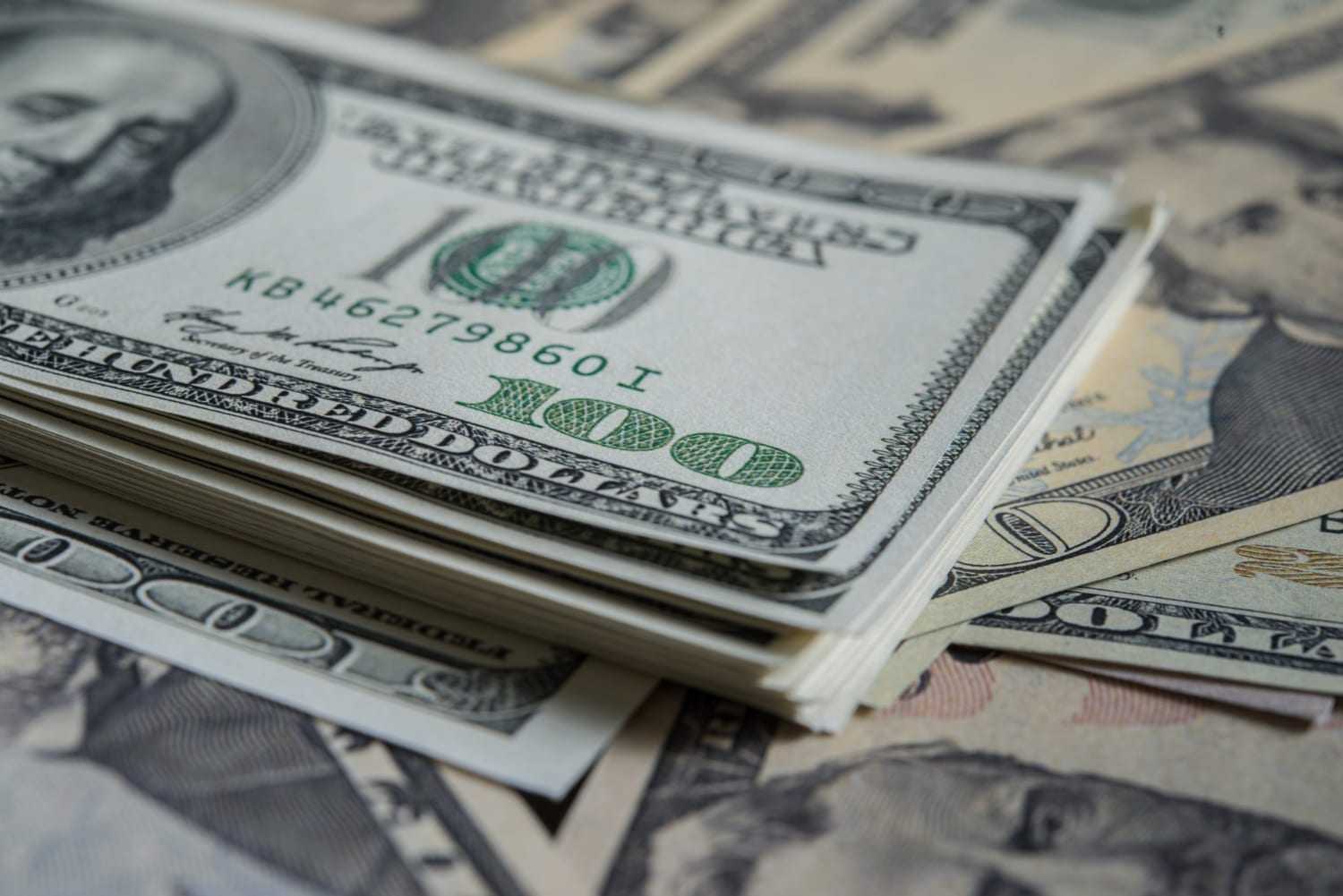 Maço de notas de cem dólares americanos sobre outras cédulas espalhadas, em foto aproximada