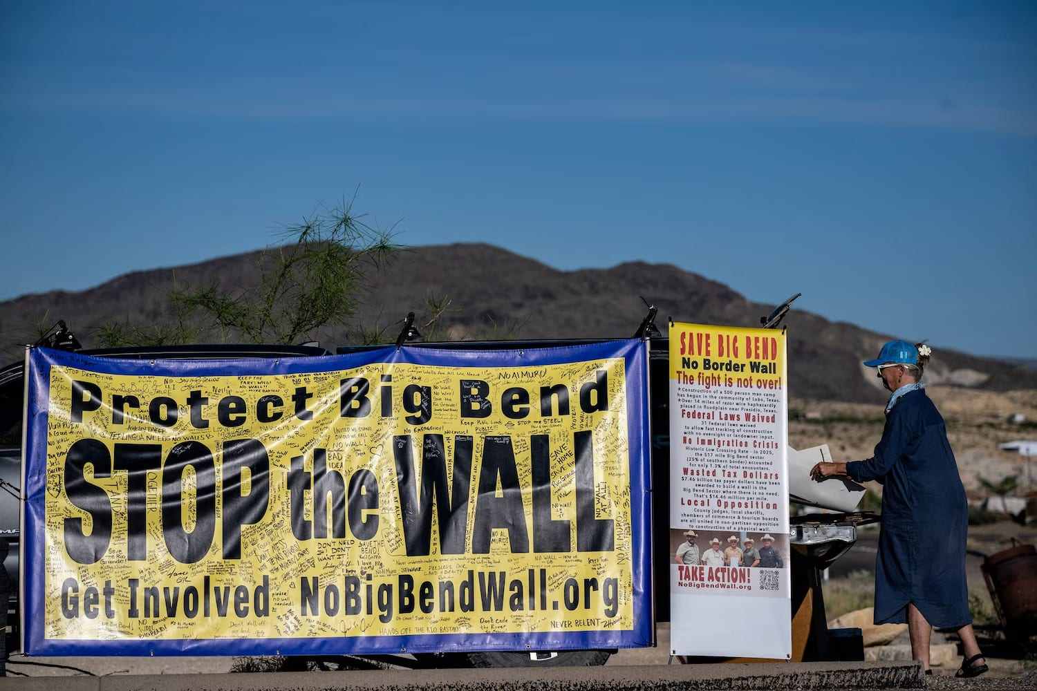 Faixa amarela e azul com os dizeres Protect Big Bend e Stop the Wall coberta de assinaturas, ao lado de um cartaz Save Big Bend, com montanhas do deserto ao fundo