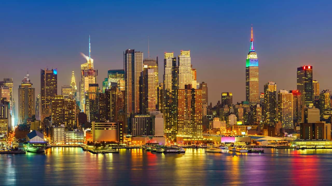 Panorama noturno da ilha de Manhattan, em Nova York, com o Empire State Building iluminado entre os arranha-céus