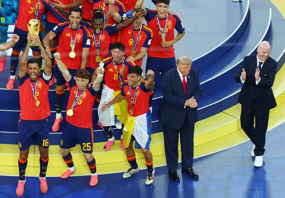 Jogadores da seleção da Espanha comemoram com a taça da Copa do Mundo no pódio, enquanto Donald Trump e o presidente da FIFA, Gianni Infantino, aplaudem ao lado