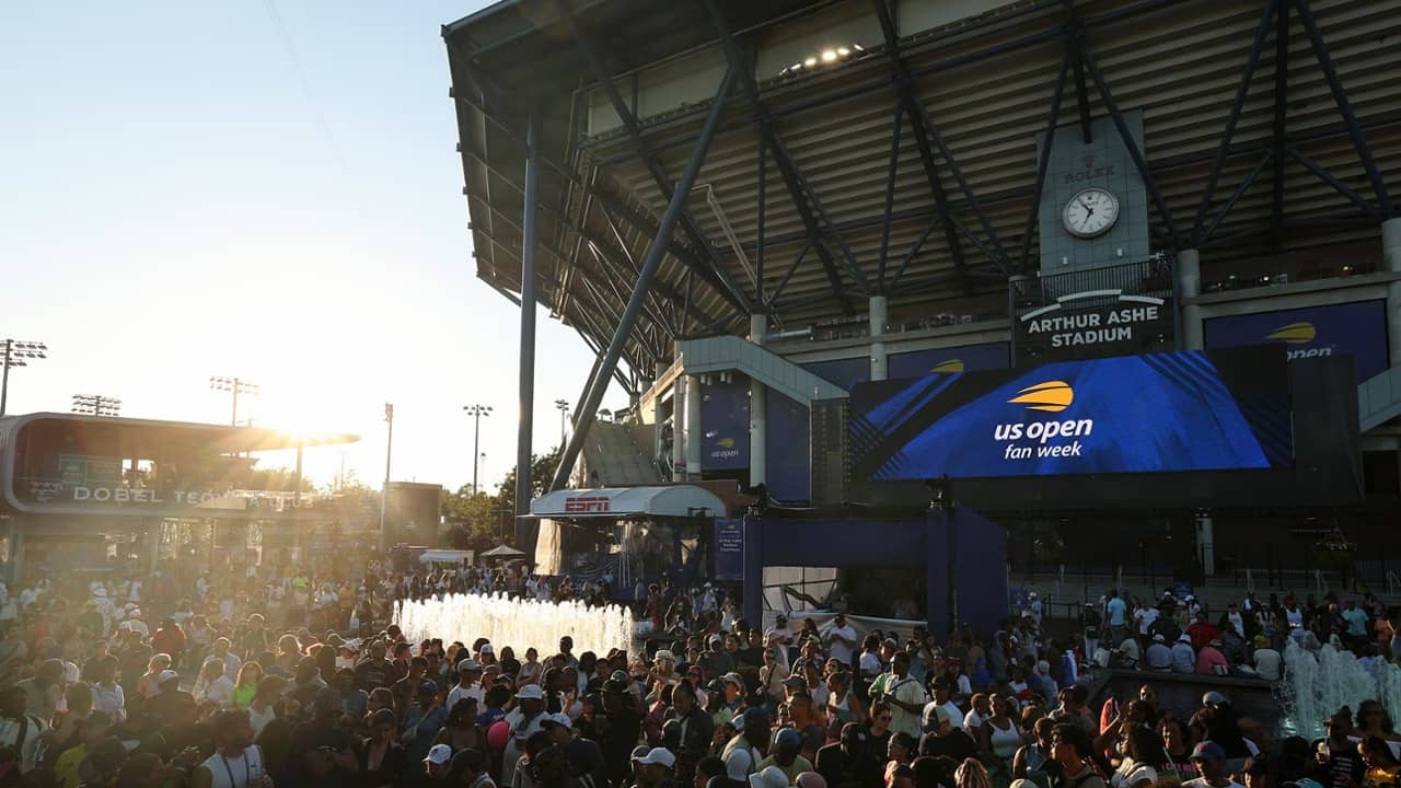 Público lotado na esplanada do Arthur Ashe Stadium, no complexo do US Open, ao lado de um chafariz e de um telão azul com a marca da US Open Fan Week