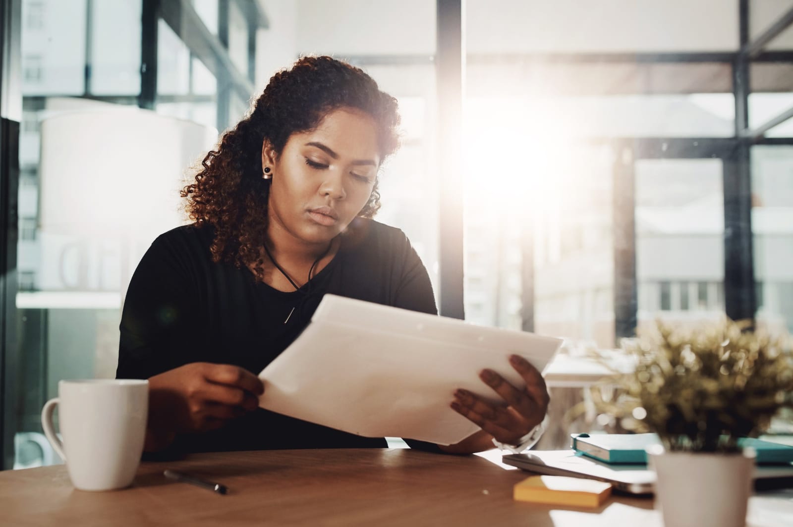 Mulher analisando documentos e envelope em um escritório iluminado pelo sol