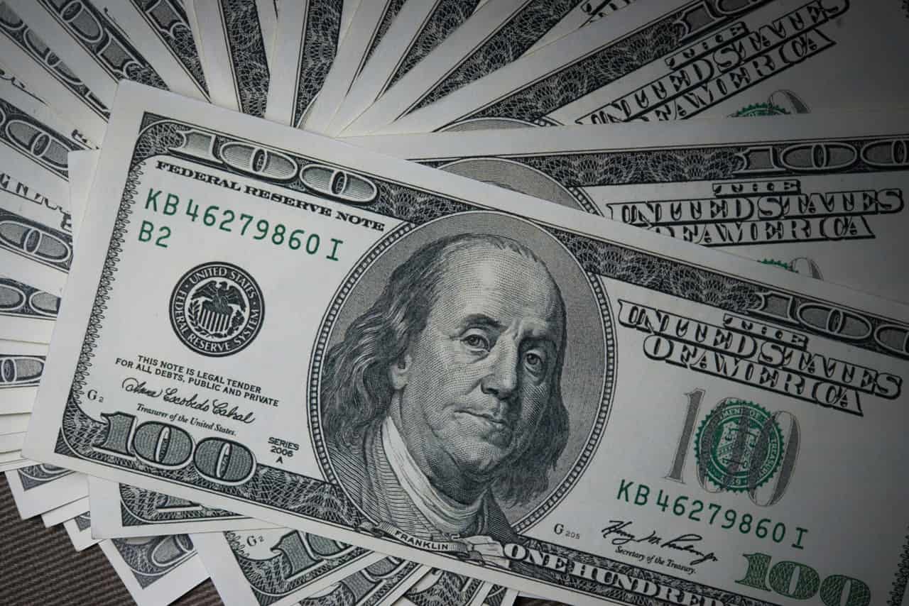 Várias notas de 100 dólares sobrepostas em leque, com o retrato de Benjamin Franklin em destaque