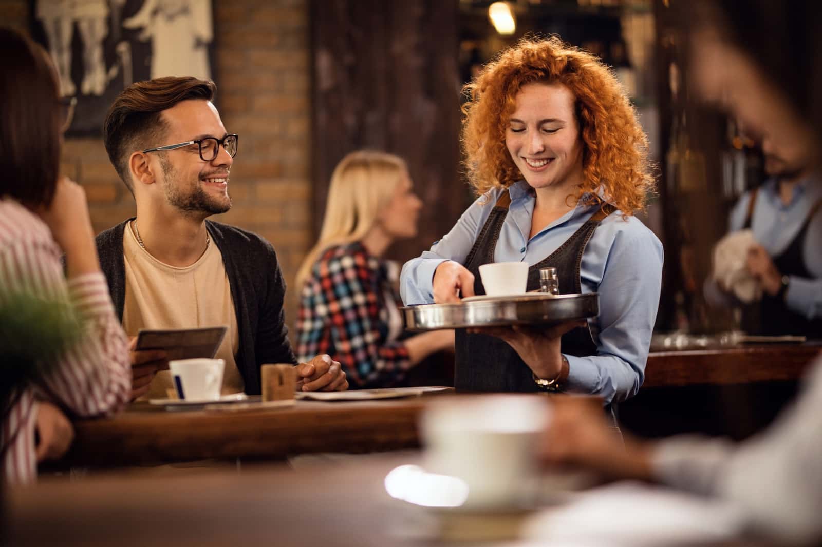 Garçonete sorridente servindo café para cliente em uma cafeteria