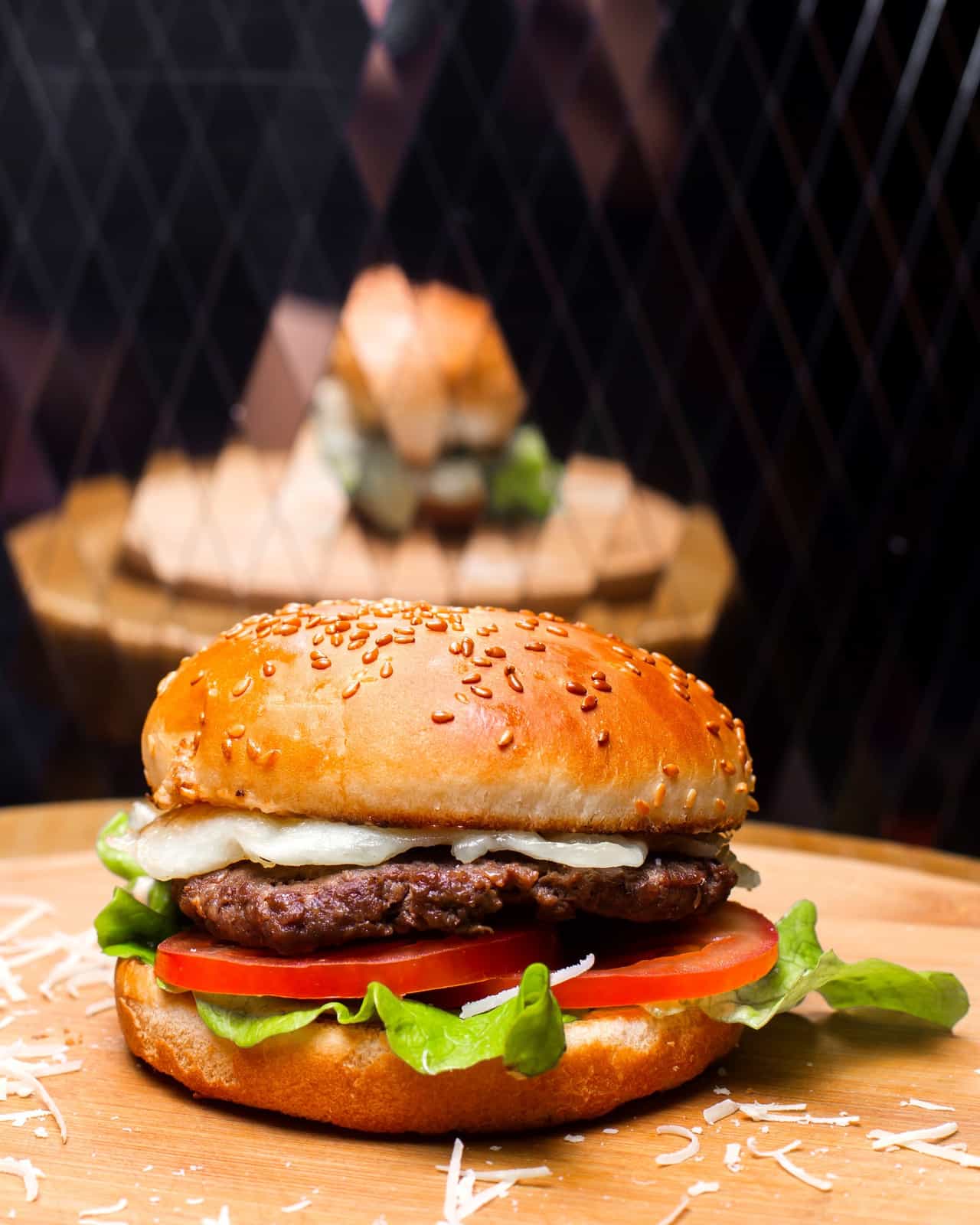 Hambúrguer com gergelim, alface e tomate em destaque sobre uma tábua de madeira