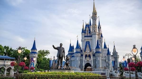 Castelo da Cinderela, no Magic Kingdom, com a estátua de Walt Disney e do Mickey em primeiro plano e canteiros de flores vermelhas