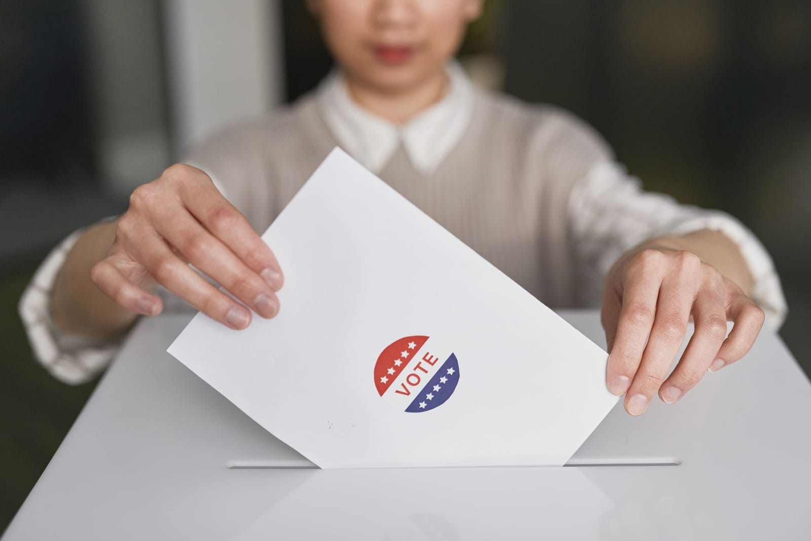 Mulher deposita uma cédula de papel com adesivo "Vote" em vermelho e azul dentro da fenda de uma urna branca