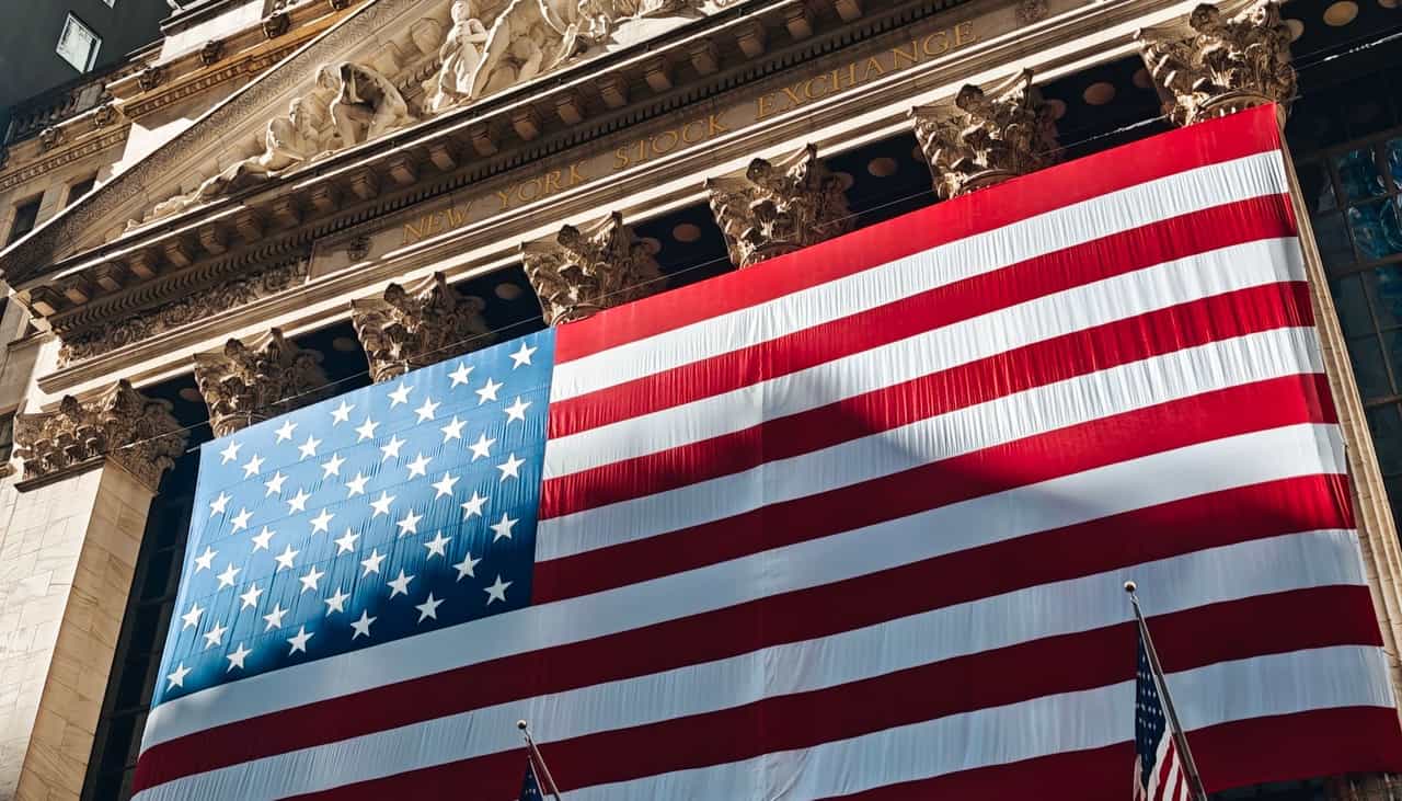 Bandeira dos Estados Unidos de grandes dimensões estendida sobre a fachada de colunas da Bolsa de Valores de Nova York