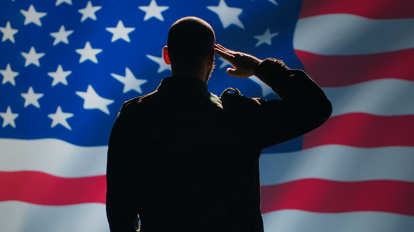 Silhueta de militar de costas fazendo continência diante de uma bandeira dos Estados Unidos iluminada