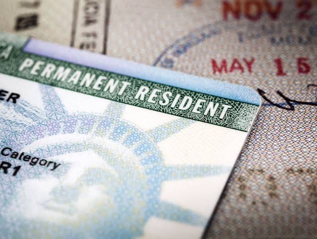 Cartão de residente permanente dos EUA, o green card, com a Estátua da Liberdade, sobre páginas de passaporte carimbadas