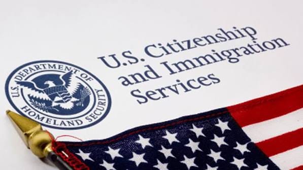 Papel com o texto U.S. Citizenship and Immigration Services e o selo do Departamento de Segurança Interna, ao lado de uma bandeira americana