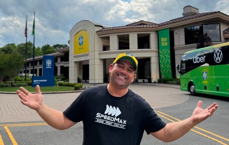 Leandro Teixeira do Vale, de camiseta da Speedmax Signs e boné do Brasil, em frente ao hotel da delegação da CBF com o ônibus da Seleção ao fundo