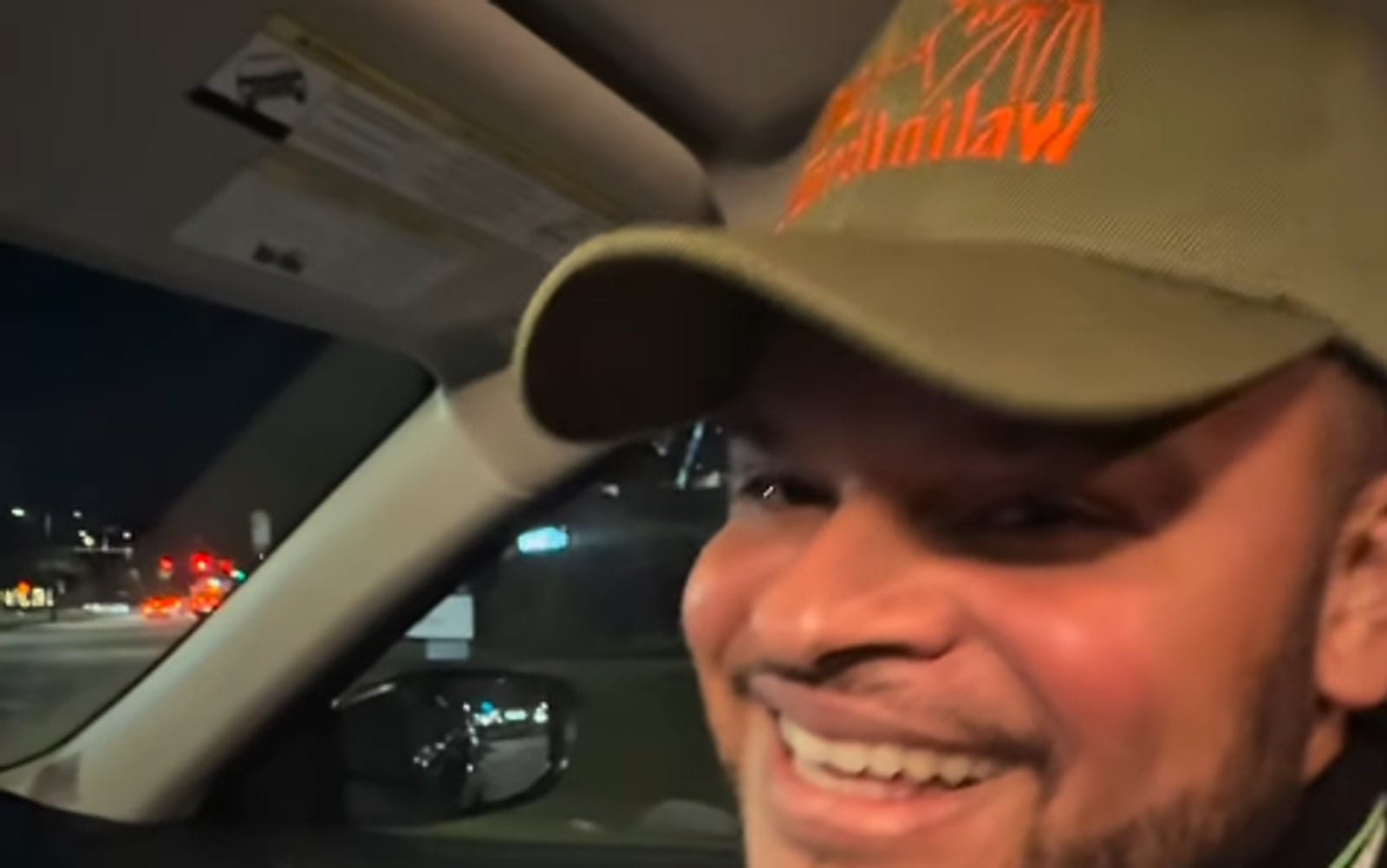 Célio Ortiz sorri dentro de um carro à noite, usando boné da GardiniLaw e segurando papéis nas mãos