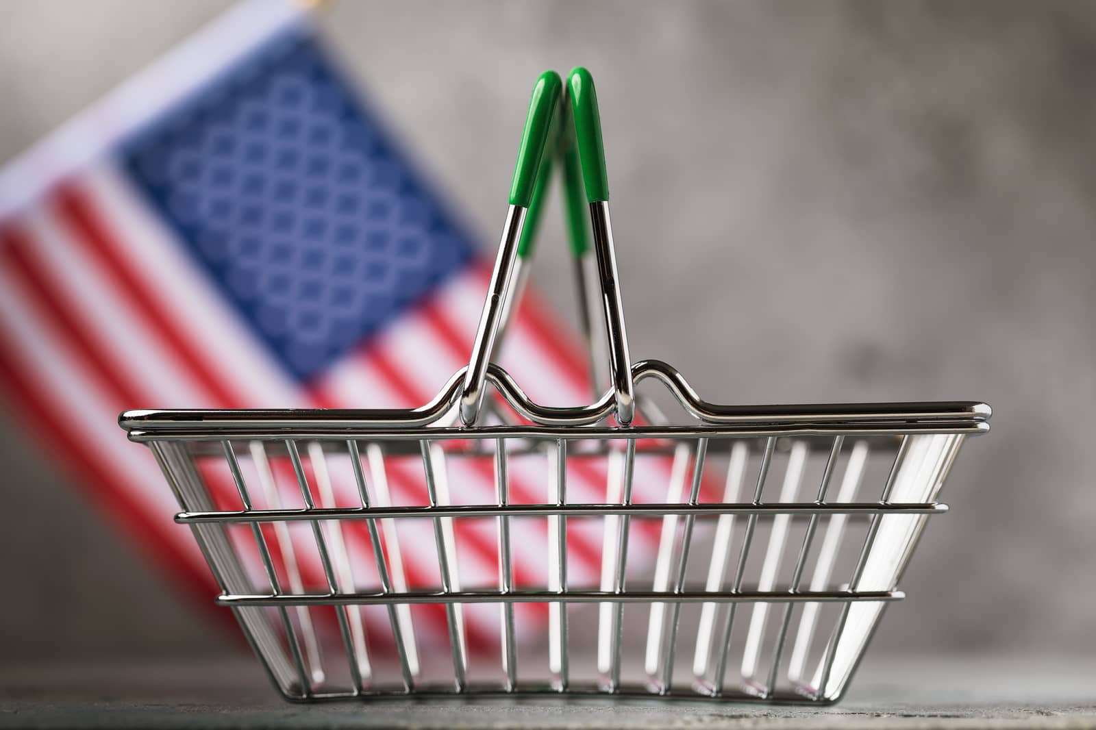 Cesta de compras vazia com bandeira dos Estados Unidos desfocada ao fundo