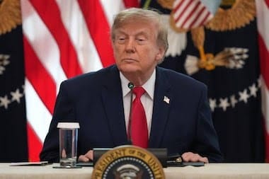 Donald Trump, de terno escuro e gravata vermelha, sentado a uma mesa diante de uma bandeira dos EUA, com o selo presidencial na frente