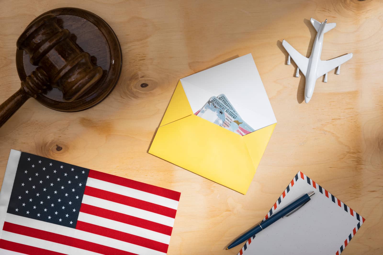 Martelo de juiz ao lado de documentos de residência permanente, bandeira americana e avião de brinquedo sobre mesa de madeira
