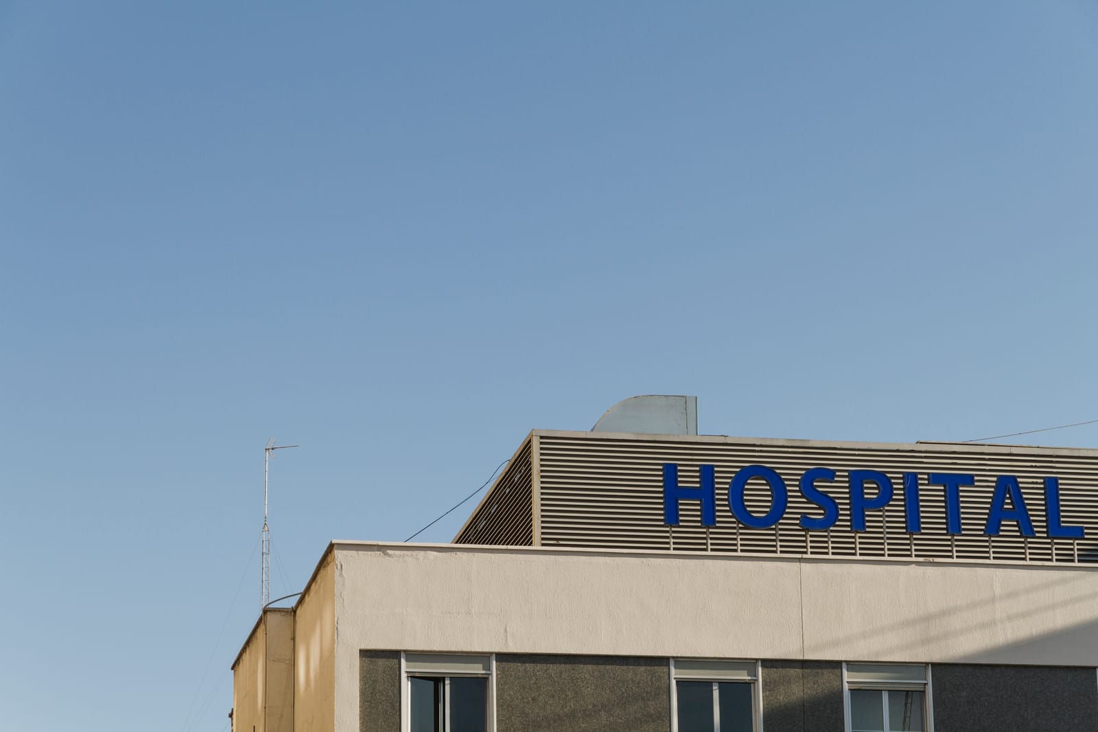 Fachada de hospital americano com letreiro azul escrito HOSPITAL contra o céu
