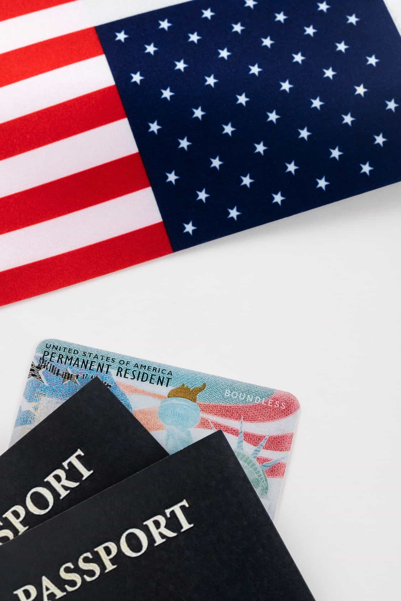 Bandeira dos Estados Unidos, um green card e dois passaportes escuros sobre uma superfície branca