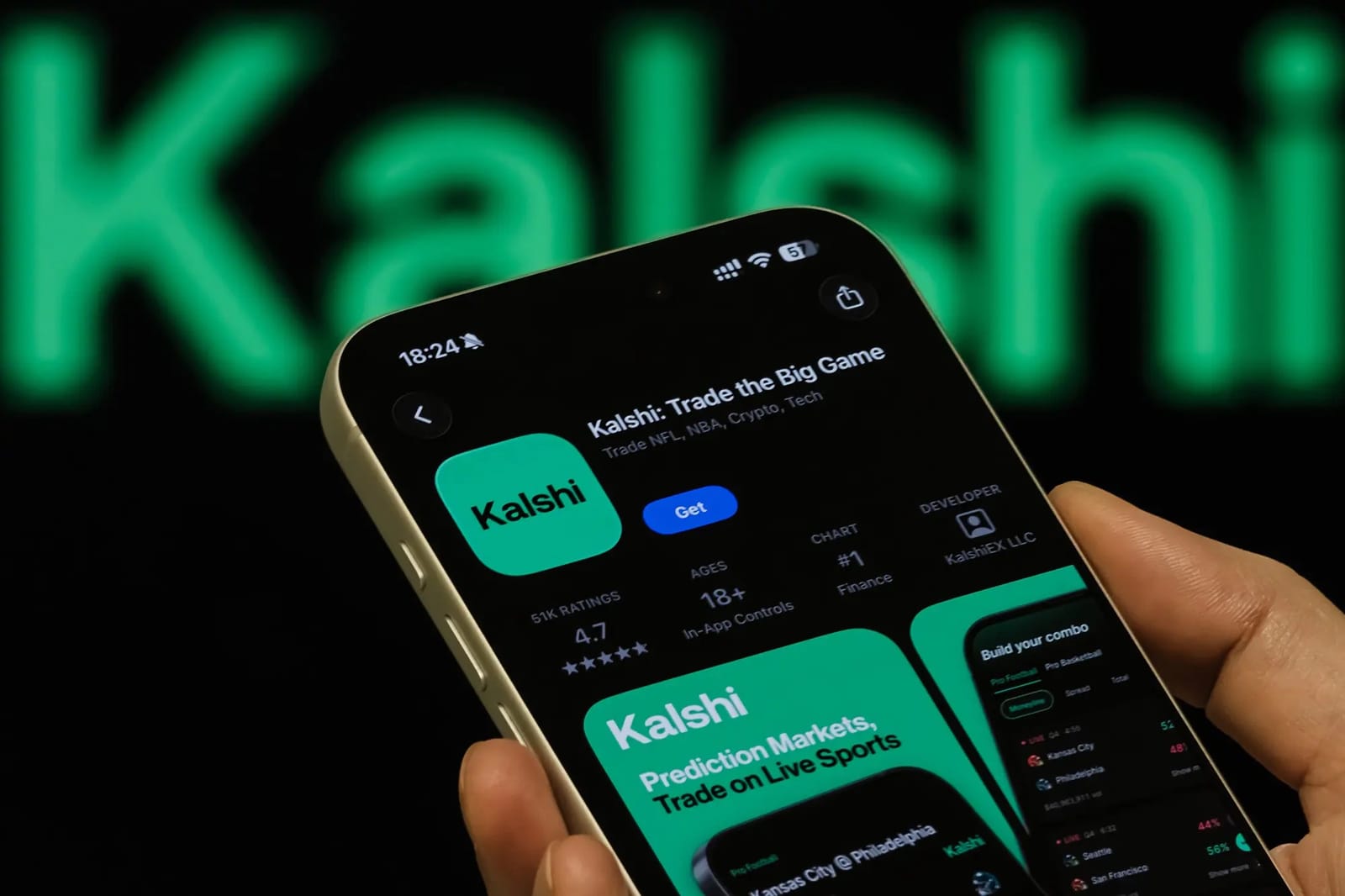 Mão segura um celular exibindo a página do aplicativo Kalshi na loja, com o nome Kalshi em verde desfocado ao fundo