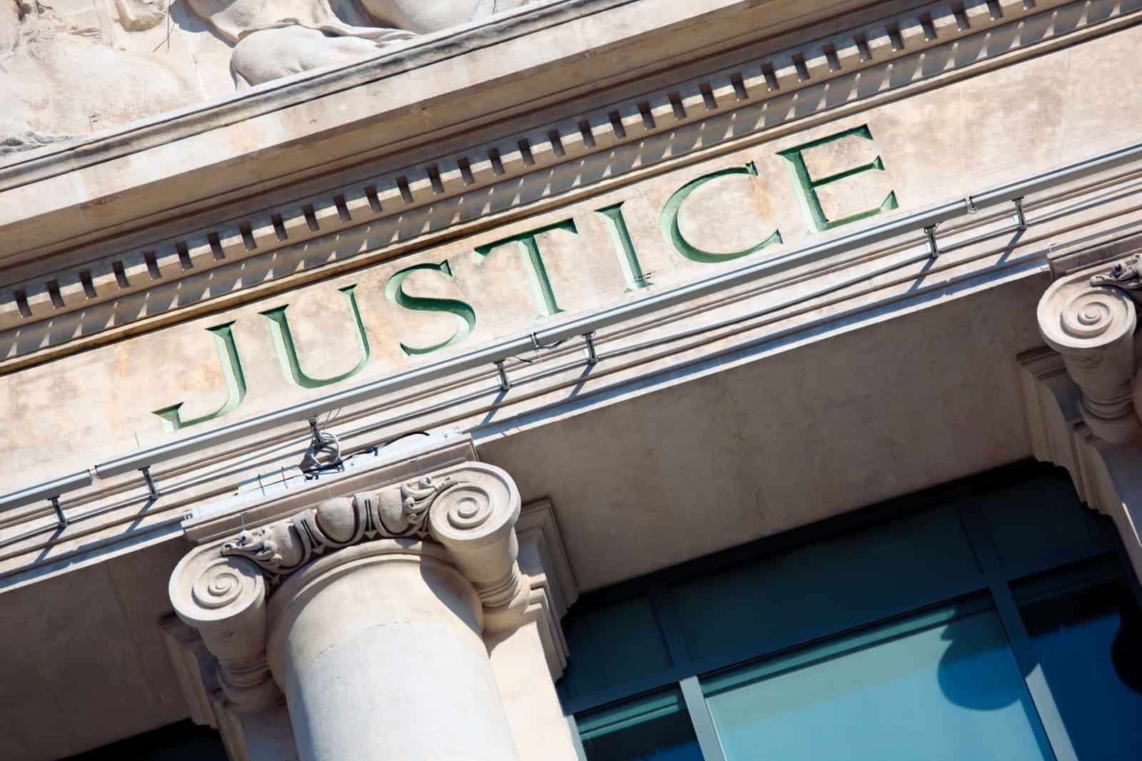 Fachada de tribunal com a palavra Justice esculpida em letras verdes na pedra