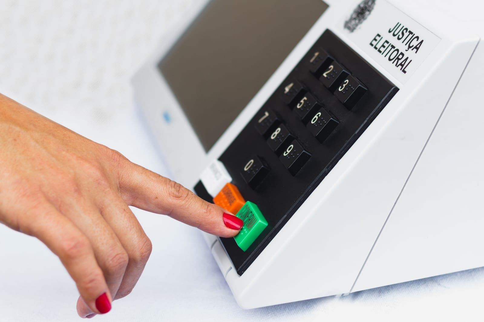 Dedo pressionando o botão confirma de uma urna eletrônica brasileira