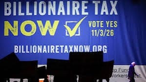 Cartaz azul com a inscrição Billionaire Tax Now, vote sim em 3 de novembro de 2026, e o endereço billionairetaxnow.org, sobre um palco